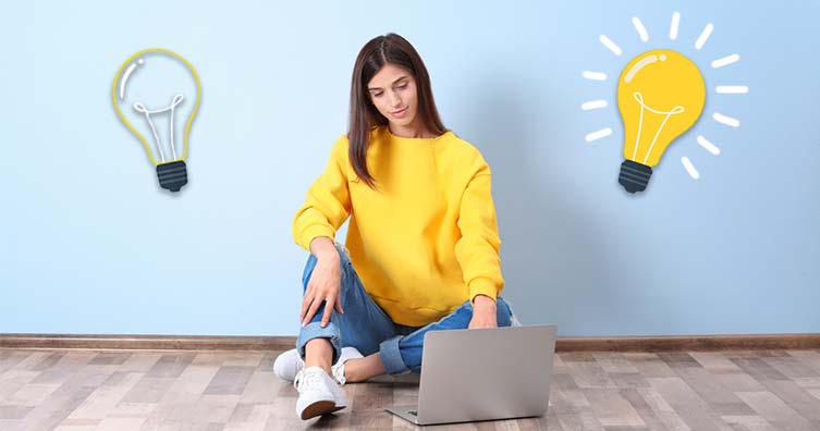 woman sitting on floor with laptop with two lightbulbs on each side