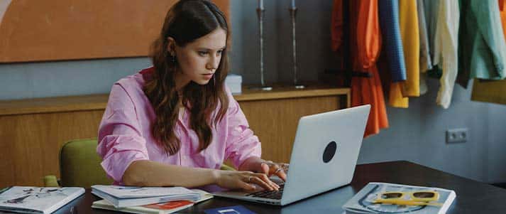 Girl working on laptop with clothes rack and design materials