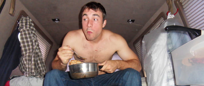 man eating out of saucepan in a van