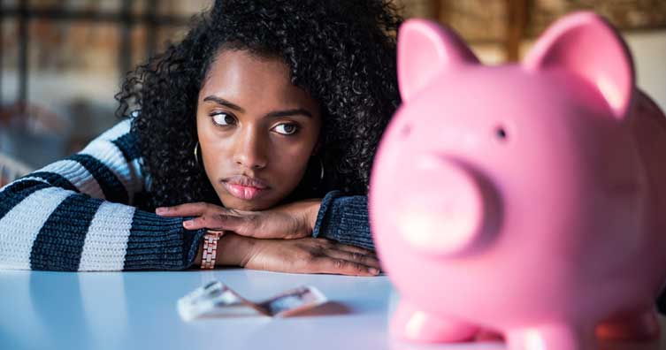 Woman looking unhappily at a piggy bank