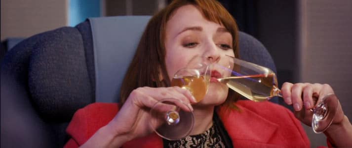 Fresh Meat character drinking champagne out of two glasses on the plane
