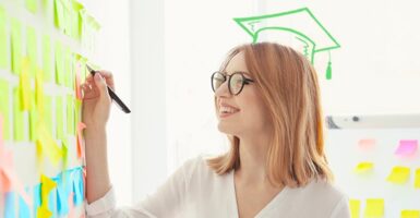 Woman writing on post it notes with drawn graduate cap