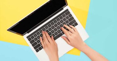 Hands on laptop keyboard with blue and yellow background