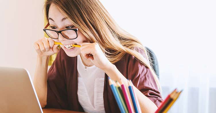woman chewing pencil by laptop