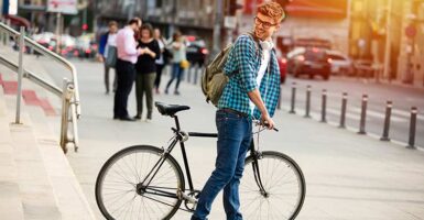 man standing in front of steps with bike looking back with headphones and backpack on