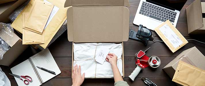 Woman doing parcel packaging with notebook and tape scissors