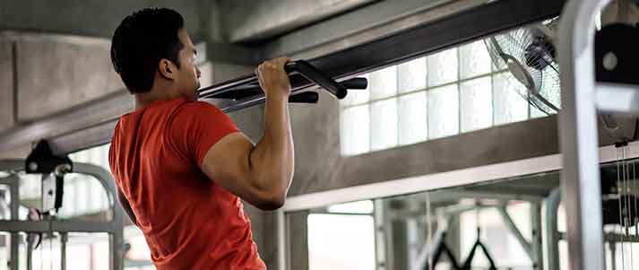 man pulls himself up in gym on pull up bar