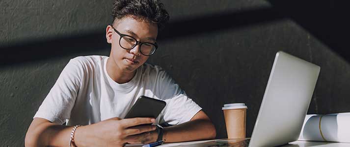 student on phone by laptop